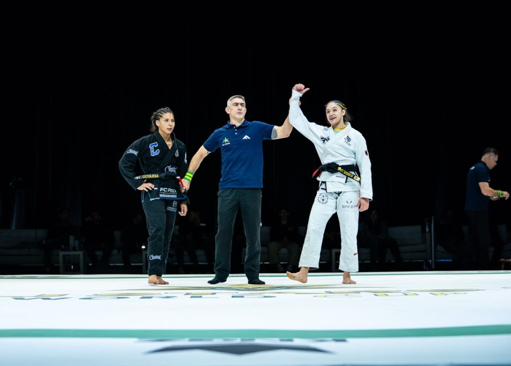 Livia Barasine has her hand raised after a dominant win over Giovanna Carneiro. Photo: @paulinhocotrim / @marianacalfatbjj